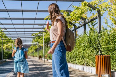Okul konseptleri, eğitim, çocukluk ve gelişim yolları da dahil olmak üzere sırt çantasıyla gezen çocuklara ebeveynler el sallıyor