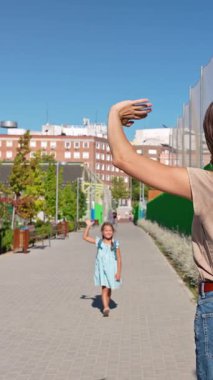 Sırt çantalı küçük mutlu bir kız annesine koşuyor ve okuldan sonra ona sarılıyor. Neşeli bir kavuşma ve sevgi dolu bir aile açık havada kucaklaşır.