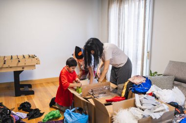 Anne ve çocuklar kostüm kutularını karıştırıyor, parti için hazırlanıyorlar. Aile eğlencesi Cadılar Bayramı için hazırlanıyor.