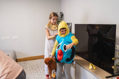 Kostümlü partiye hazırlanan iki çocuk, Mısır firavunu kıyafeti giyerken erkek kardeşine balık kostümü için yardım eden kız kardeş.