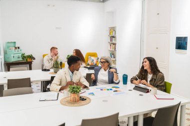 Aydınlık bir ofiste yapılan toplantı sırasında iş stratejisi ve mali grafikleri tartışan farklı yaş ve etnik köklerden profesyonel ortaklar