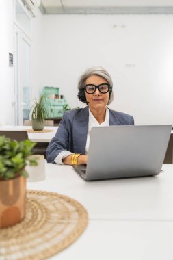 Modern bir çalışma alanında kıdemli bir kadın uzak bir işte çalışıyor, online bir toplantıya veya webinar 'a katılıyor