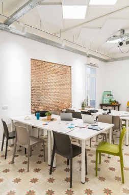 Büyük bir masa, sandalyeler, cihazlar, açık tuğla duvar ve akustik paneller içeren parlak, boş çalışma odası