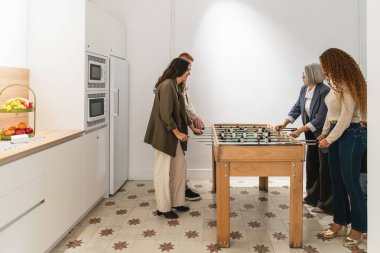 Çeşitli profesyonel meslektaşlar modern ofiste bir iş molası sırasında eğlenceli bir masa futbolu oyunu oynuyorlar.