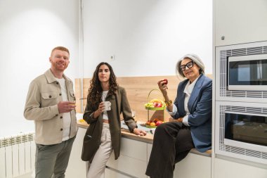 Yaş ve cinsiyet farklılığı olan üç çok ırklı profesyonel, birlikte çalışan parlak bir mutfakta mola verdiklerinde rahatlıyor ve iletişim kuruyorlar.