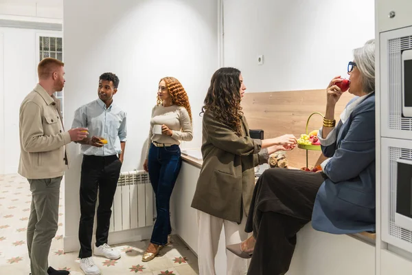 İş arkadaşları, modern ortak ofis mutfağında bir mola sırasında etkileşim ve atıştırmalık yiyerek işbirliği ve takım oluşturmayı teşvik ediyorlar.