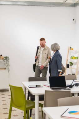 Aydınlık, açık bir planda yürüyen ve sohbet eden iki farklı meslektaş ofisi paylaşıyor ve pozitif bir çalışma ortamı yaratıyor.