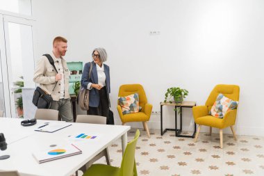 Çağdaş bir çalışma alanına girerken ya da çıkarken konuşan çeşitli iş arkadaşları, konforlu bir bekleme alanı sunuyor