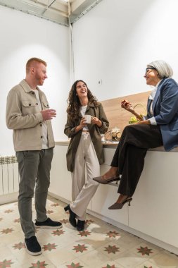 Çeşitli meslektaşlar modern bir mutfak alanında kahve molası sırasında birlikte gülüp rahatlıyorlar.