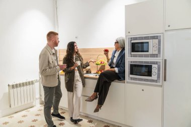 Çeşitli meslekdaşlar gündelik bir sohbeti paylaşıyor, modern bir mutfak alanında mola veriyor. İletişim güçlendiriliyor