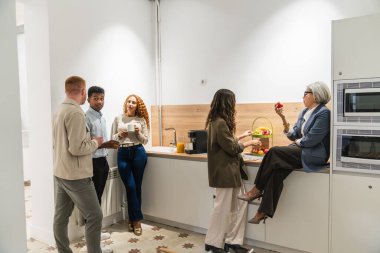 Bir grup farklı meslektaş parlak bir mutfakta durmuş içki ve meyvelerle sohbet ediyor ve eğleniyorlar.