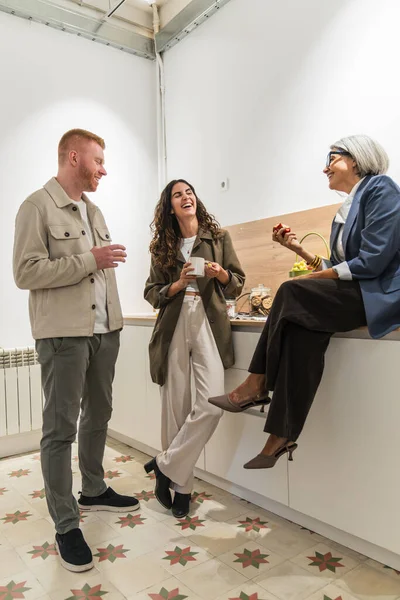 Çeşitli meslektaşlar modern bir mutfak alanında kahve molası sırasında birlikte gülüp rahatlıyorlar.