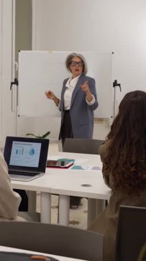 Kendine güvenen üst düzey yönetici meslektaşlarına sunum yapıyor, tahtaya yazı yazıyor ve modern bir ofiste stratejiyi tartışıyor.