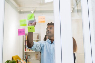 Genç adam takım üyeleriyle işbirliği yapıyor, iş stratejileri planlıyor parlak, modern bir çalışma ofisinde renkli yapışkan notlar kullanıyor.