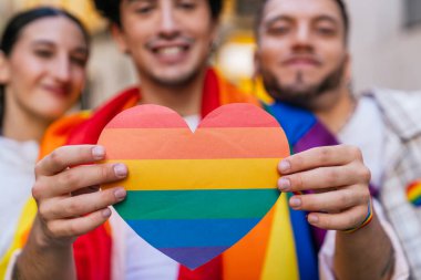 Gururu kutlayan neşeli insanlar, ellerinde gökkuşağı bayraklı bir kalp, aşkı, çeşitliliği ve lgbtq toplumunu simgeliyor.