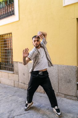 Şehrin caddesinde dans eden hevesli genç adam güçlü hip hop hareketlerini canlı sarı bir duvara karşı ifade ediyor.