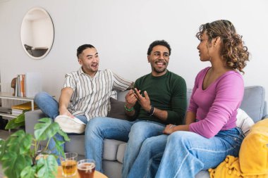 Çeşitli arkadaş grupları evde birlikte vakit geçiriyorlar, kanepede oturuyorlar, sohbetin ve sosyal toplantının keyfini çıkarıyorlar.