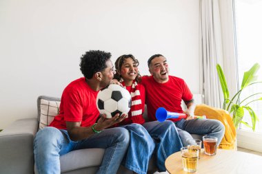 Çeşitli arkadaş grupları spor izlerken bir futbol topu ve vuvuzela tutarak kutlama ve heyecan hissediyorlar.