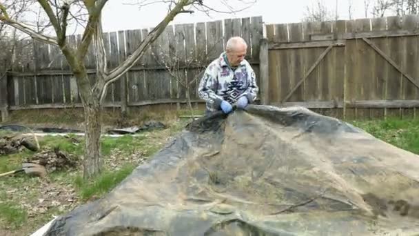 Oudere man bereidt waterdichte bescherming van grond — Stockvideo