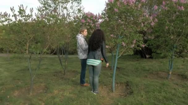 Δύο κορίτσια sniffing ιώδη λουλούδια στο καταπράσινο πάρκο — Αρχείο Βίντεο
