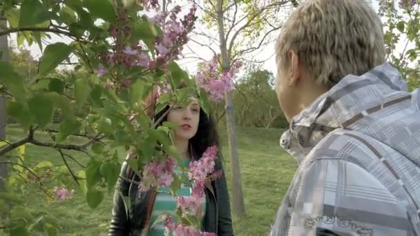 Duas meninas cheirando flores lilás no parque verde — Vídeo de Stock