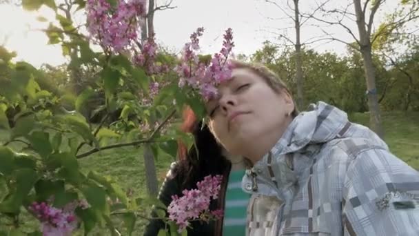 Dos chicas oliendo flores lila en el parque verde — Vídeos de Stock