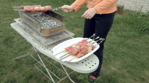 Girl puts barbecue skewers with meat on brazier — Stock Video