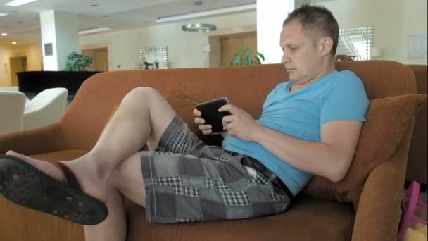 Ein Mann liegt auf seinem Mittelteil-Tablet auf einer Couch — Stockvideo