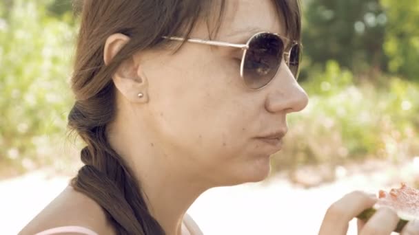 Улыбающаяся женщина летом ест арбуз на открытом воздухе — стоковое видео