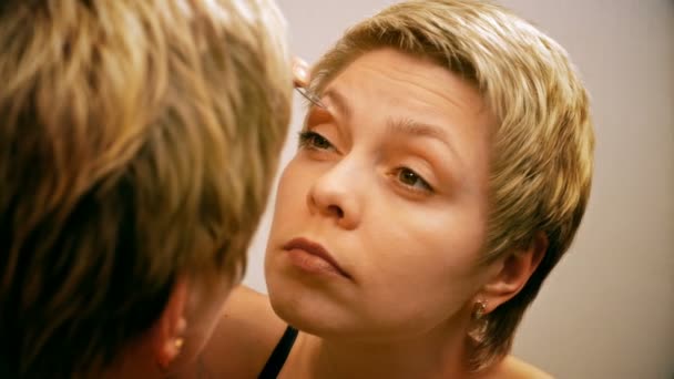 Frau zupft und zieht vor Spiegel ihre Augenbrauen heraus — Stockvideo