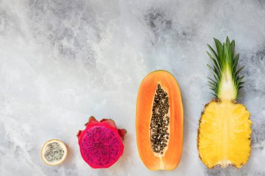 Gri arka planda tropik meyveler. Ananas, papaya, ejderha meyvesi, çarkıfelek meyvesi.