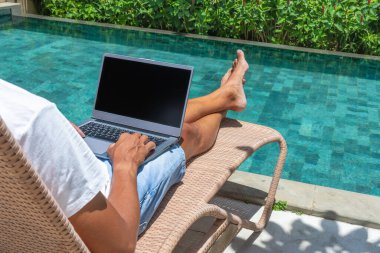 A man works online with a laptop by the pool. Freelance, work in nature.