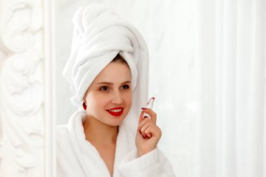 Kadın duştan sonra otel banyosunda dudaklarını boyuyor. Aynayla ilgili sabahlık giymiş Slav görünümlü güzel bir kadın. Mutlu bayan. Sağlıklı yüz derisi. Sevimli kız yüzünü yıkadı ve duygularını gösterdi.