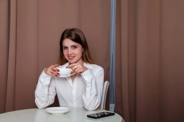 Dziewczyna Słowiańskim Wyglądzie Telefonem Białym Kubkiem Siedzi Przy Stole Kobieta — Zdjęcie stockowe