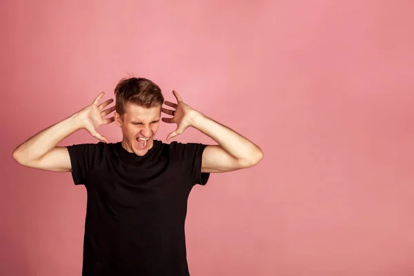 Emotional scared man has scared fright on pink background. Gesture of person speaks of horror and hysteria, this is unpleasant for him. Young male who shouts and gestures with his hands. Copy space