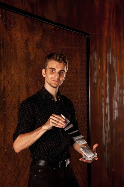 Portrait of young man with gambling cards at gate. Handsome guy shows tricks with card. Clever hands of magician on brown texture background. Concept of entertainment and Hobbies. Copy space