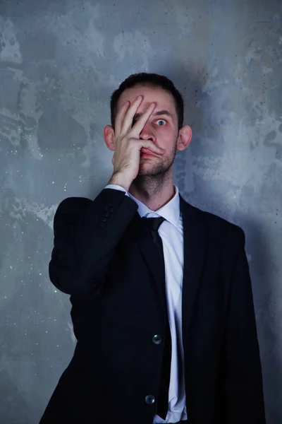 Depressed young man in suit depicts horror and fear on gray textured background. Gesture of person speaks speaks of fear and hysteria, it is unpleasant for him. Concept of human emotion. Copy space