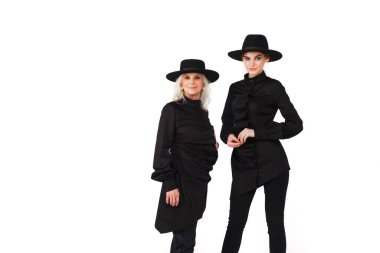 Tarz sahibi genç ve yaşlı iki iş kadını, siyah şık takım elbiseli, beyazların üzerinde tek başına duruyor. Kameraya poz veren şık elbiseli kadınlar. Tarz, moda, güzellik ve hedeflerin başarısı kavramı