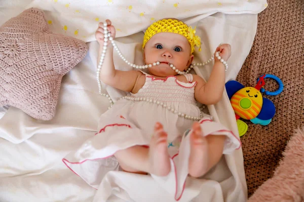 可爱的蓝眼睛6个月大的白衣女孩在床上玩珍珠珠子 漂亮的金发美女迷人的孩子在特写中表现出感情 健康儿童和养育子女的概念 — 图库照片