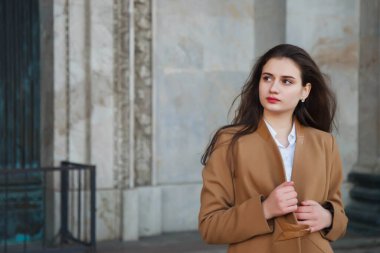 Kahverengi ceketli, şık, genç ve şık bir kadın sokakta yürüyor. Gülümseyen, mutlu ve maksatlı kadınlar için sonbahar modası. Tarz, moda, güzellik ve başarı hedefleri. Boşluğu kopyala