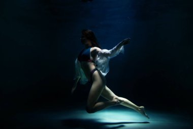 Slender pretty young woman brunette in bathing suit and white blouse in dark pond, illuminated by moonlight. Elegant female underwater. Concept of beauty, tenderness and striving for ideal. Copy space clipart