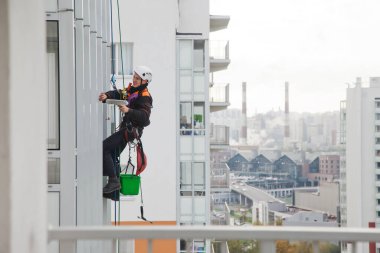 Endüstriyel dağcılık işçisi dış cephe camlarını yıkarken konut binasının üzerinde asılı duruyor. İp erişimi olan işçi ev duvarında asılı. Şehir işleri kavramı. Boşluğu kopyala
