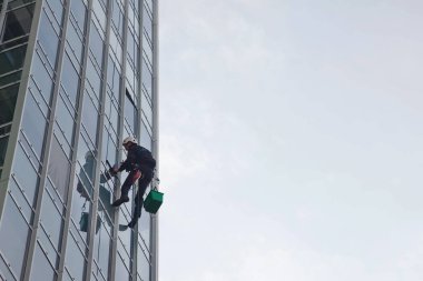 Endüstriyel dağcılık işçisi dış cephe camlarını yıkarken konut binasının üzerinde asılı duruyor. İp erişimi olan işçi ev duvarında asılı. Şehir işleri kavramı. Boşluğu kopyala