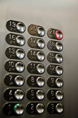 Asansördeki zemin düğmeleri 21 numara 21 'e basılı. Asansör hareketleri için krom kontrol paneli çok katlı binada. Trafik, ulaşım. Asansör duvarında bir sürü düğme var.