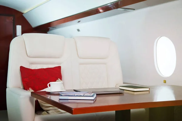 Laptop, diary and cup of coffee on table of luxury interior in private jet. Modern and comfortable business airplane with decor. Concept of passenger service quality in aviation industry, at highest