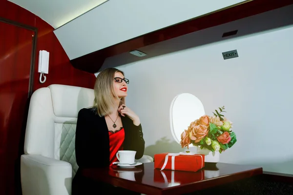 Cute young businesswoman with gift flying in luxury private jet. Business woman in airplane first class seat during trip. Concept quality of passenger service in aviation industry, travel at highest