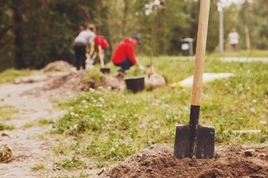 Genç, evli, iş üniformalı, yerde kürek ağacı fidanı olan bir çift. Toprağın seçkinleştirilmesi için arka plan. Peyzaj, doğa, çevre ve ekoloji kavramı. Boşluğu kopyala