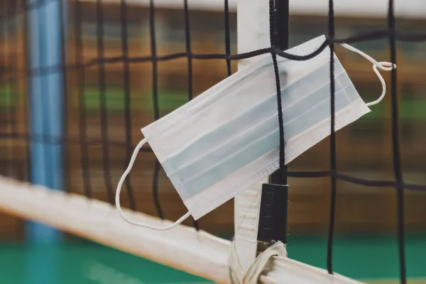 Medical mask in volleyball net in an old empty sports hall with referee tower. Background for team volleyball game. Concept of getting sport, lifestyle and success during period pandemic. Copy space