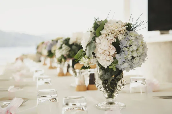 Wedding table decor with flowers in fresh air on background of sea. Floral decoration for decoration of parties and dinners. Serving for holiday, event, party or reception in restaurant. Copy space