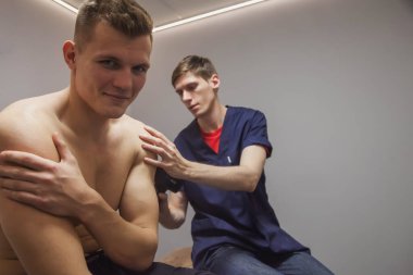 Masaj terapisti, profesyonel bir erkek sporcunun yaralanmasını tedavi ediyor. Spor salonunun tıbbi ofisinde spor tabancası şok masajı. Atletik vücut masajı için perküsyon terapisi. Fizyoterapi